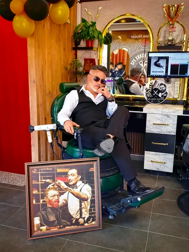 Ümit Bekar, Efe Erkek Kuaförü'nde yeşil berber koltuğunda otururken; yanında Van Gogh ve Dalí tablosu